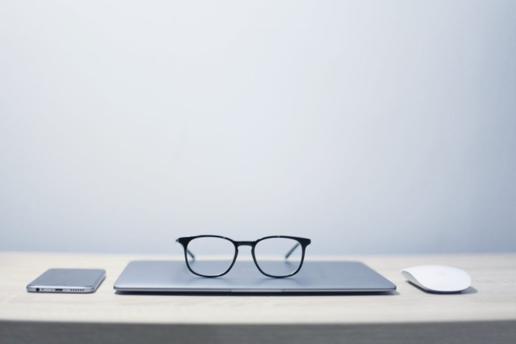 Desk with phone, mouse, laptop and glasses