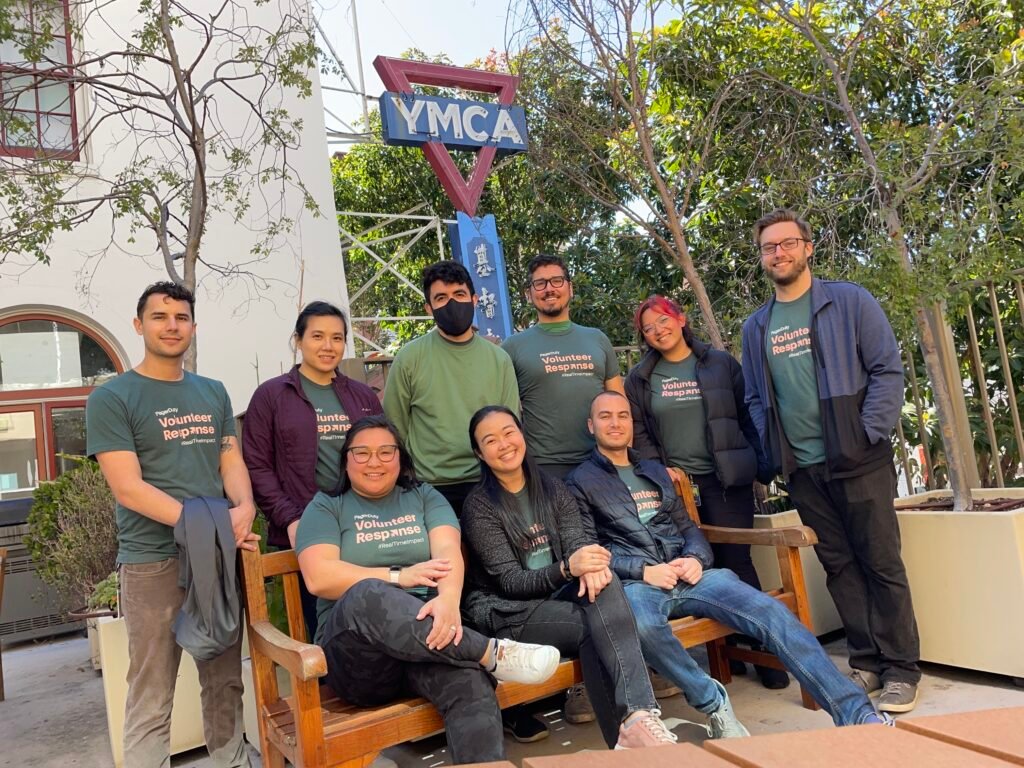 Image of nine people in front of YMCA sign; six people standing behind a bench and three people sitting on a bench