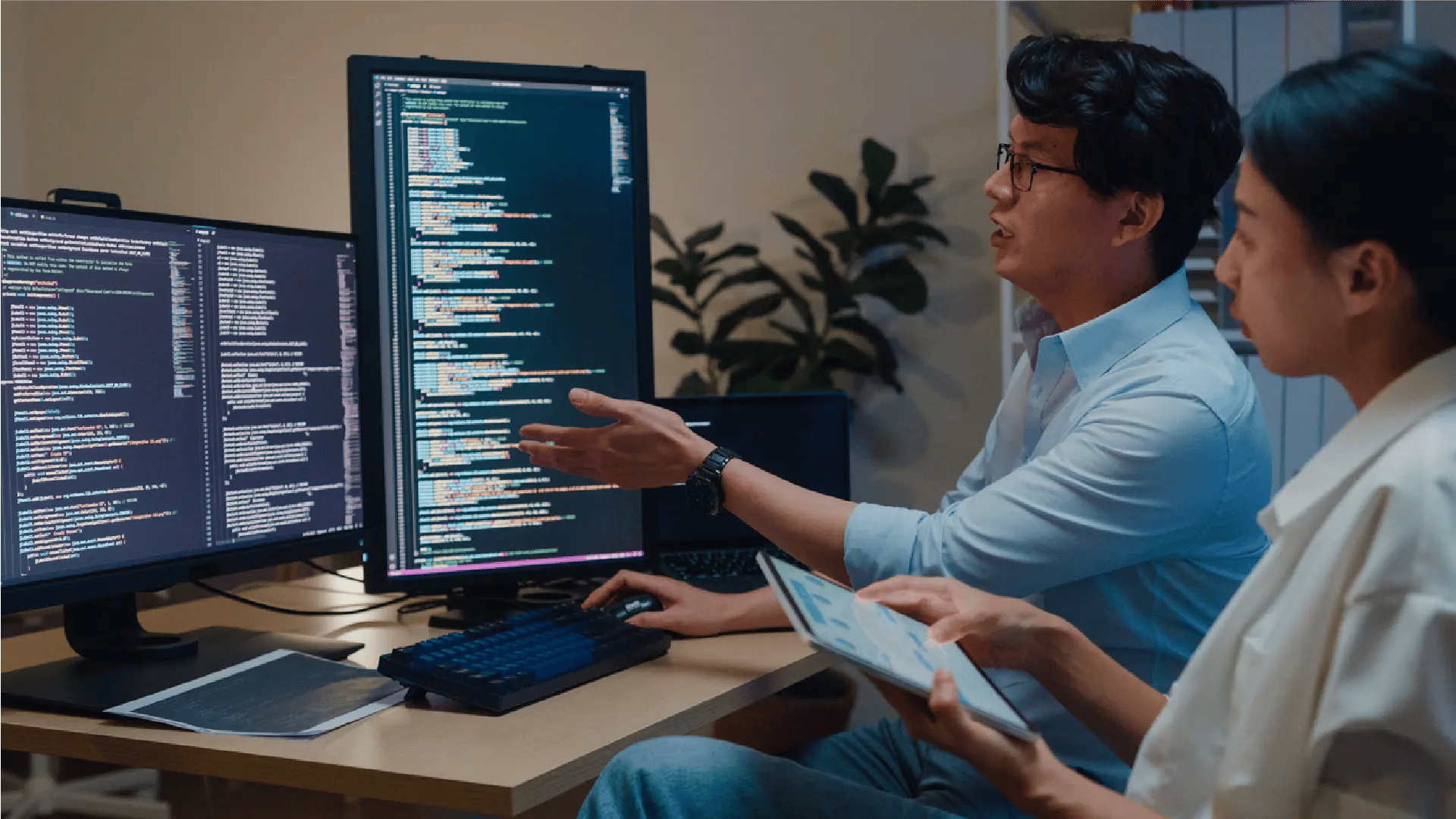 Man checking tablet in front of larger screen of figures